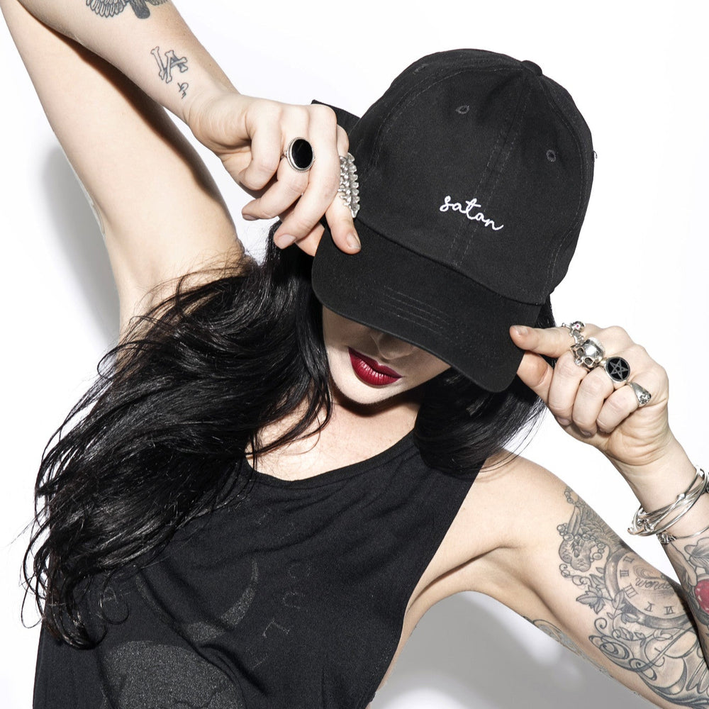 A model wearing a classic black hat with satan on the front.