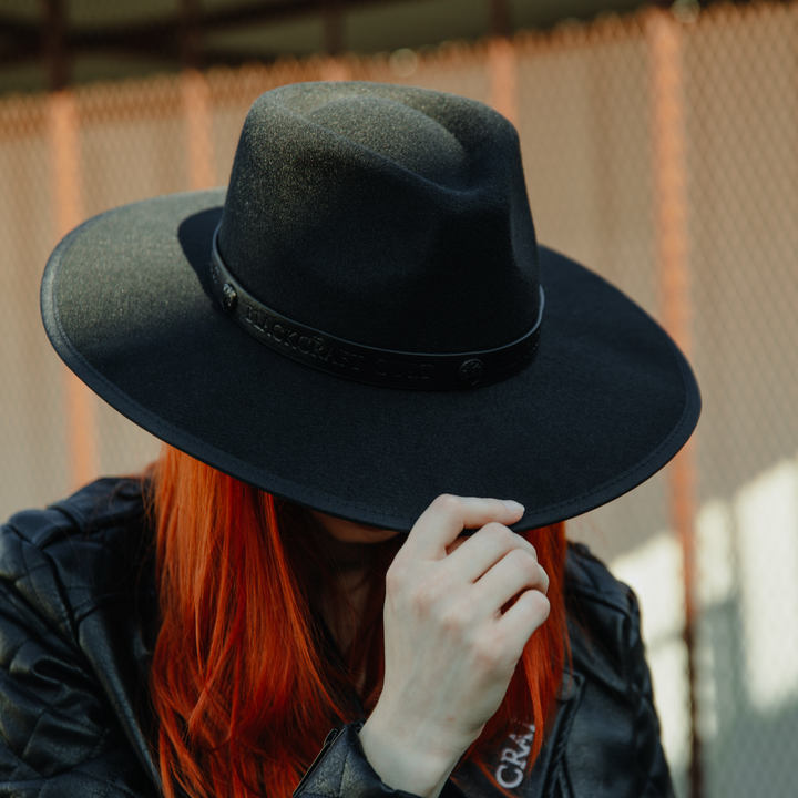 A model wearing a black wide brimmed fedora hat.